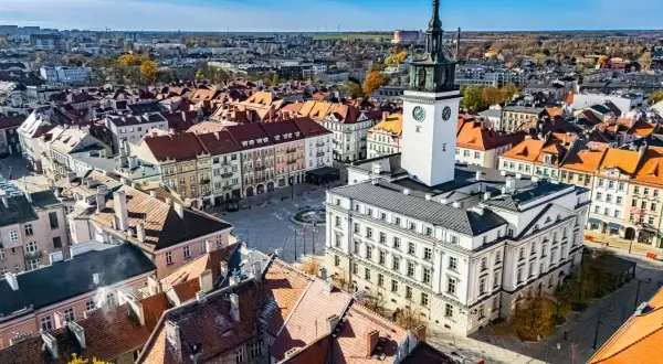 Widok na rynek z ratuszem i wieżą zegarową w najstarszym mieście w Polsce. Dachy kamienic i błękitne niebo.