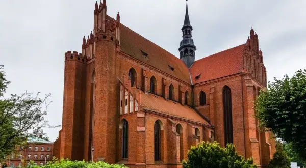 Imponująca ceglana katedra w Pelplinie z charakterystyczną wieżą i strzelistymi dachami, otoczona zielenią.
