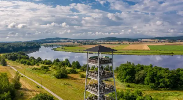 Wieża widokowa nad jeziorem, otoczona zielenią i polami uprawnymi.