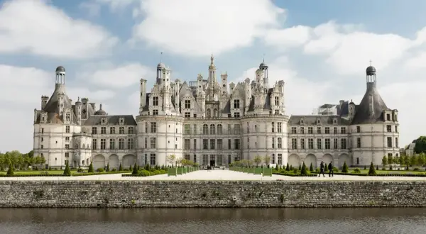 Majestatyczny zamek Chambord z licznymi wieżyczkami i kopułami, odbijający się w spokojnej wodzie.