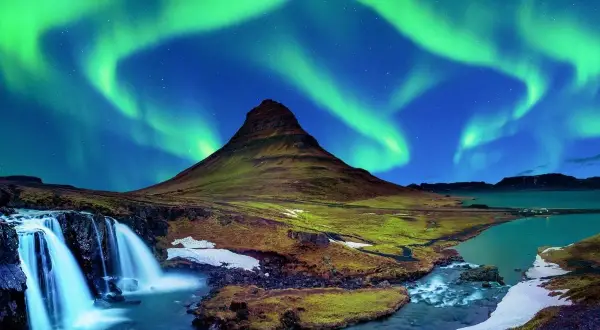 Spektakularna zorza polarna nad górą Kirkjufell, ikoną Islandii. Wodospad i rzeka dopełniają ten magiczny krajobraz.