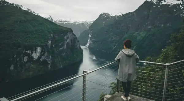 Kobieta podziwia majestatyczne fiordy norweskie. Woda lśni, a wodospad spływa po zboczu góry.