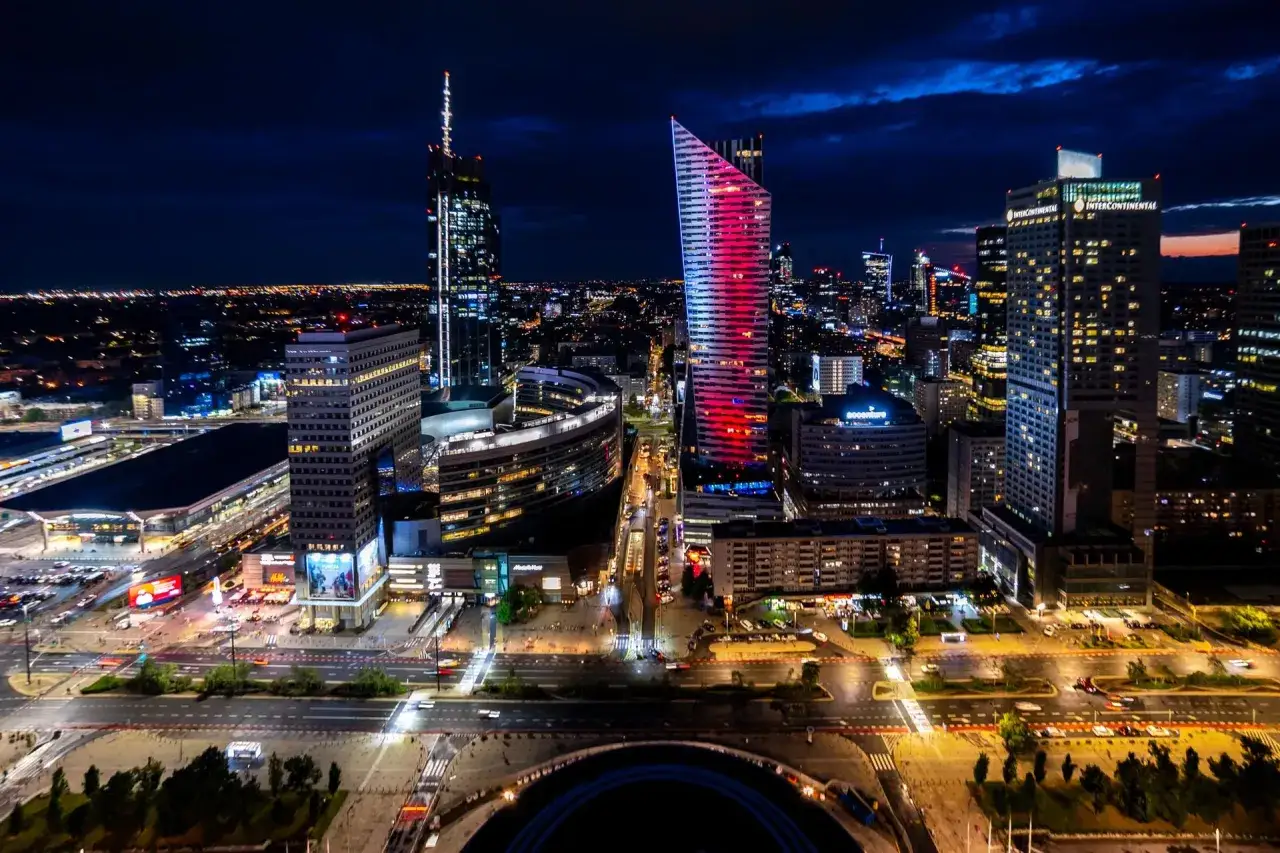 Nocny widok na nowoczesne centrum Warszawy, jednego z największych miast w Polsce. Oświetlone wieżowce i ulice tworzą spektakularny krajobraz.