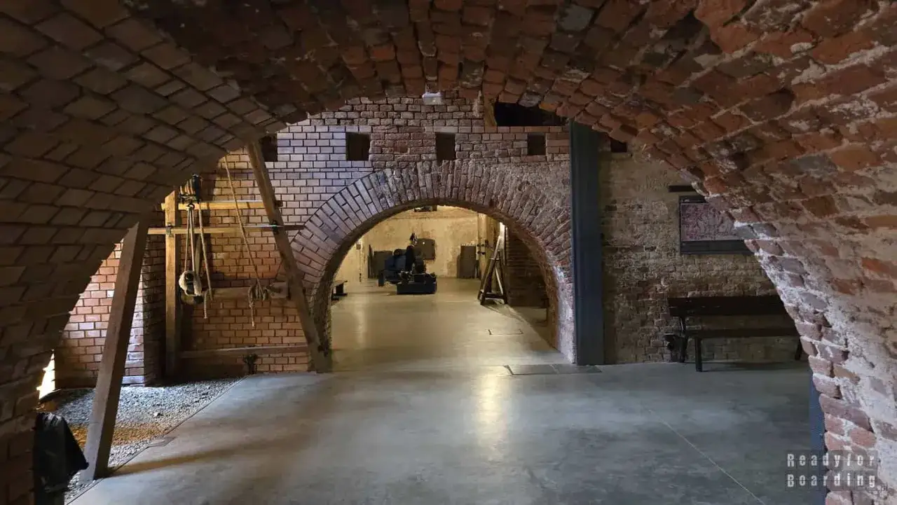 Wnętrze zabytkowych kazamatów z ceglanymi łukami i ekspozycją historyczną.